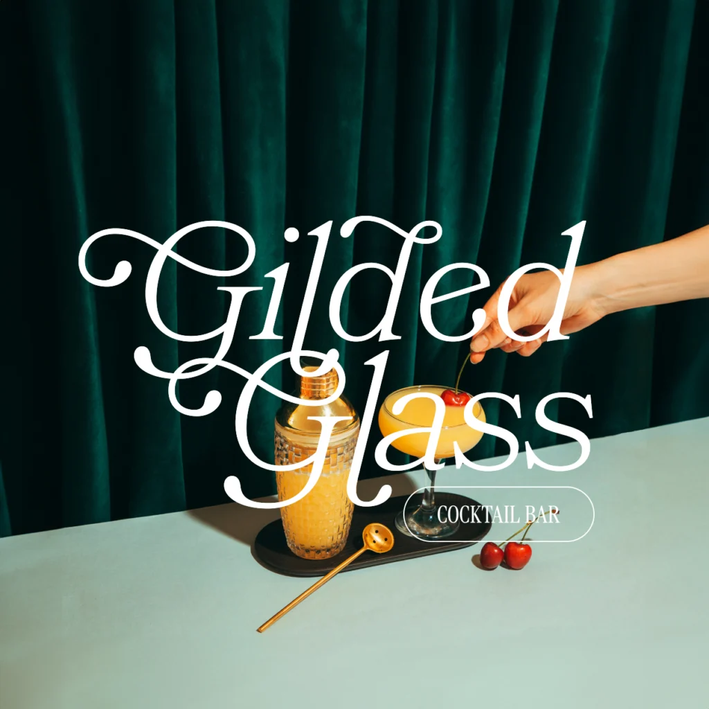 Gilded Glass Cocktail Bar brand identity design. This is a logo mockup with a hand dipping a cherry into a glass of mimosa in front of a vintage green velvet curtain. The logo is placed in the front.